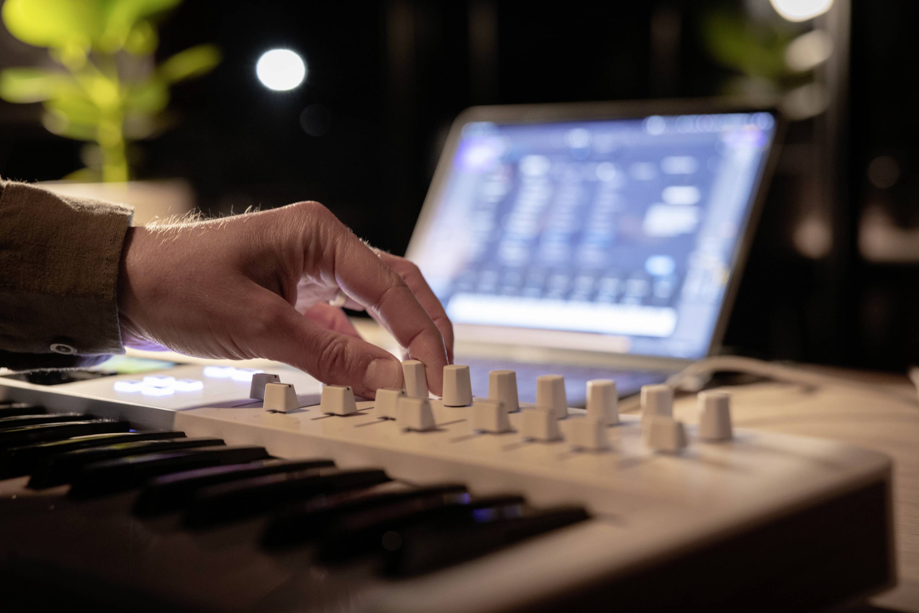 Eine Hand bedient einen Drehregler an einem Musik-Controller. Im Hintergrund ist ein Laptop mit geöffneter Musiksoftware sichtbar.