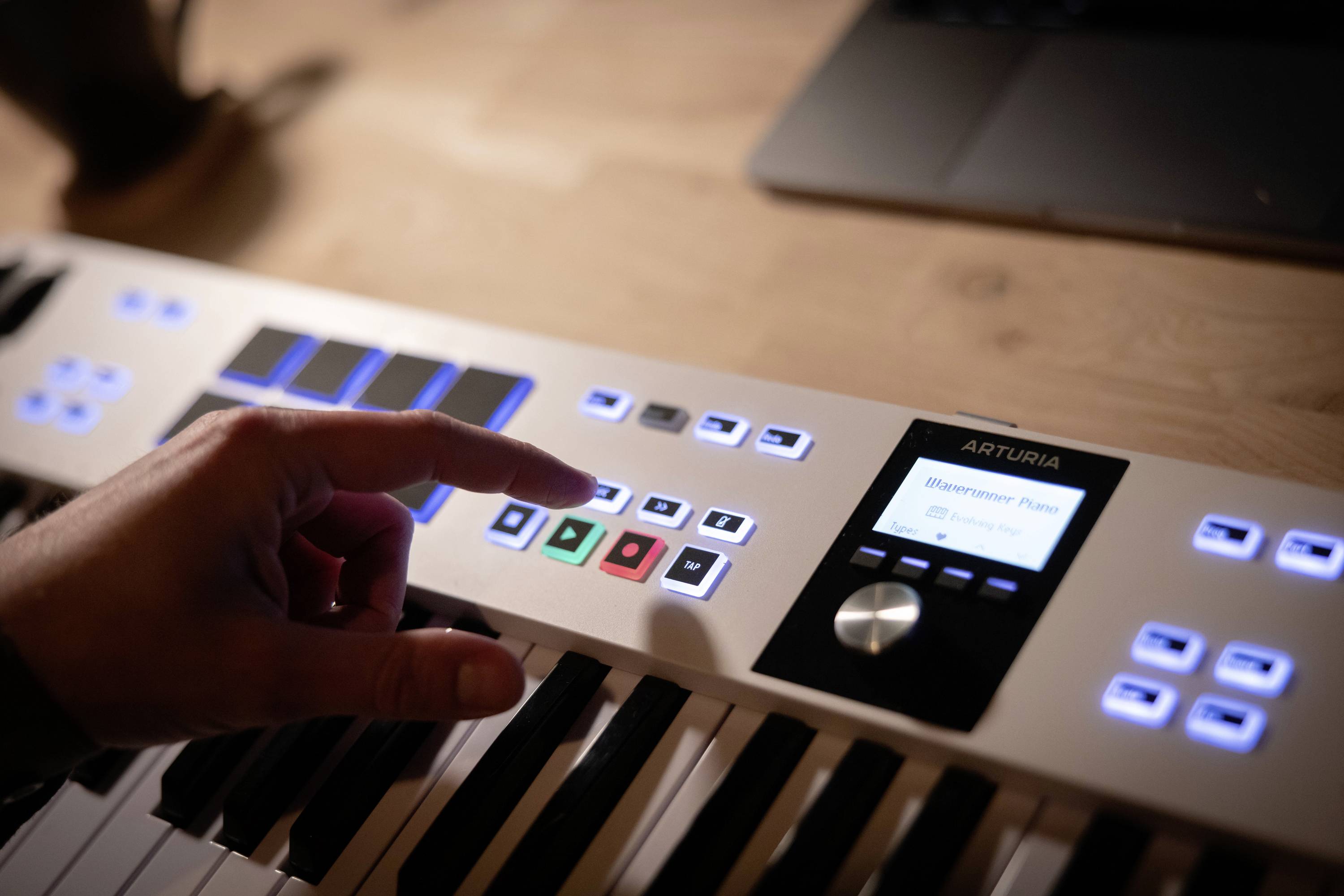 Eine Hand drückt eine Taste auf einem MIDI-Keyboard. Ein Bildschirm zeigt 'Microprism'. Ein Laptop steht im Hintergrund.