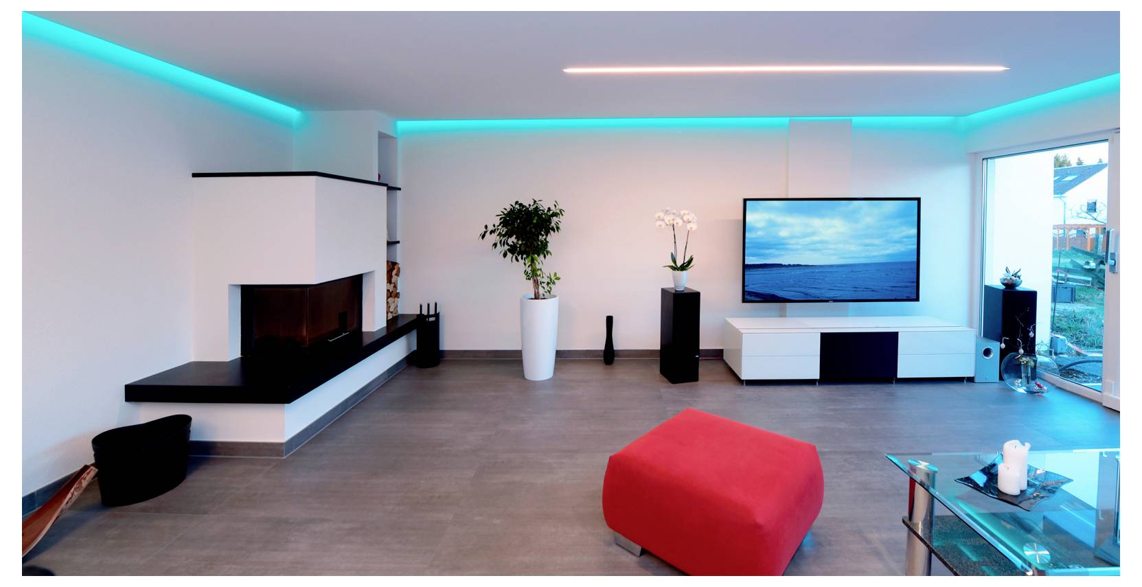 Modernes Wohnzimmer mit Eckkamin, Wand-TV, weißen Schränken, Pflanzen, blauer LED-Deckenbeleuchtung und einem roten Hocker im Vordergrund.