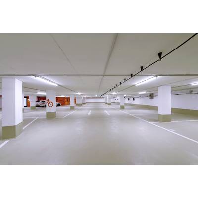 Leerer, beleuchteter Parkplatz in einem Parkhaus mit Pfeilen auf dem Boden, die die Fahrtrichtung anzeigen.