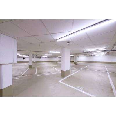 Parkhaus mit leeren Stellplätzen, weißer Decke und markierten Parklinien. Deckenleuchten erhellen den Raum, eine Kamerasicht erscheint links.