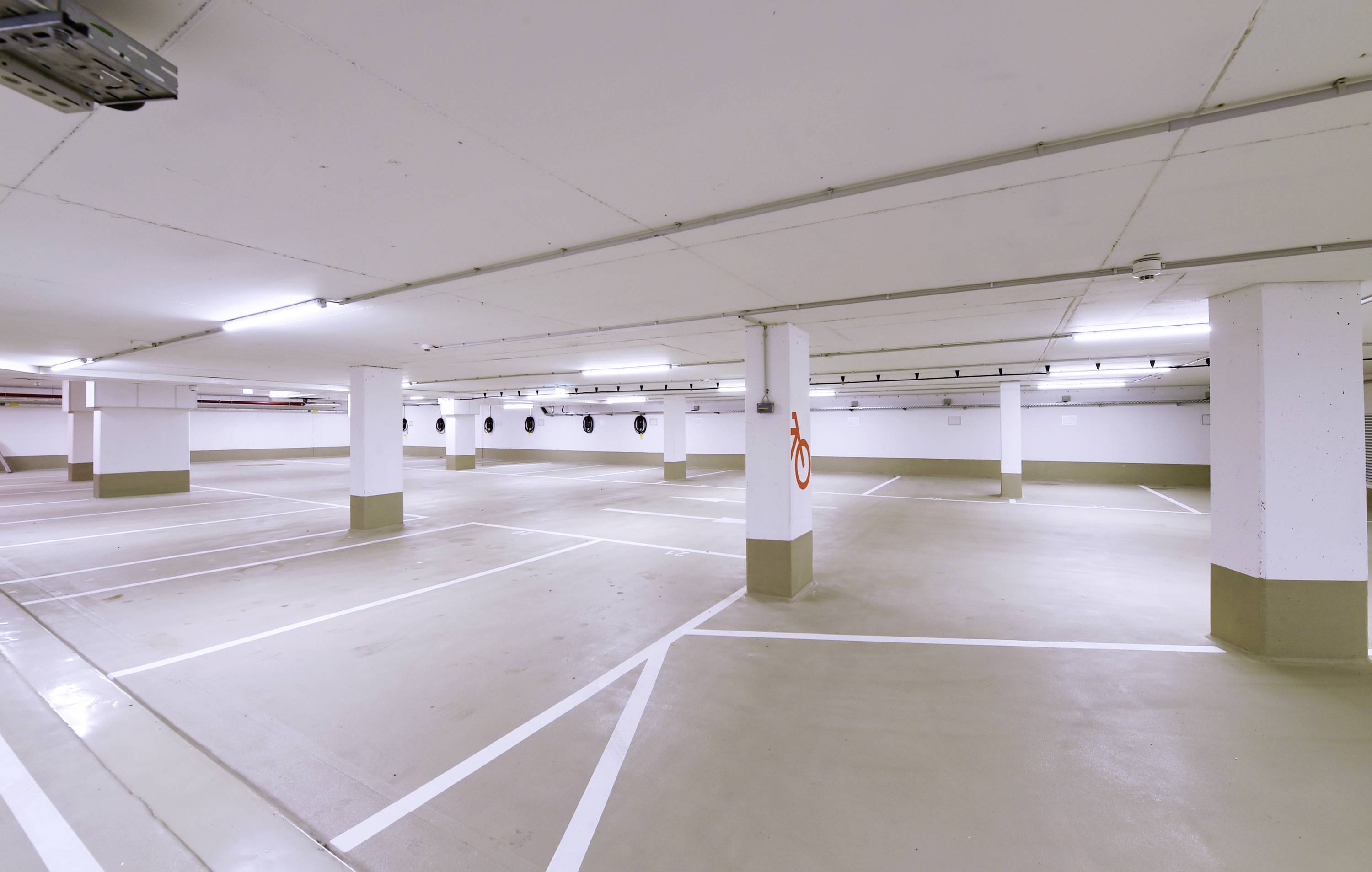 Leerer, gut beleuchteter Parkplatz in einer Tiefgarage mit markierten Stellplätzen und einem Feuerlöscher an der Wand.