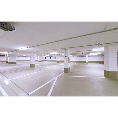 Leerer, gut beleuchteter Parkplatz in einer Tiefgarage mit markierten Stellplätzen und einem Feuerlöscher an der Wand.