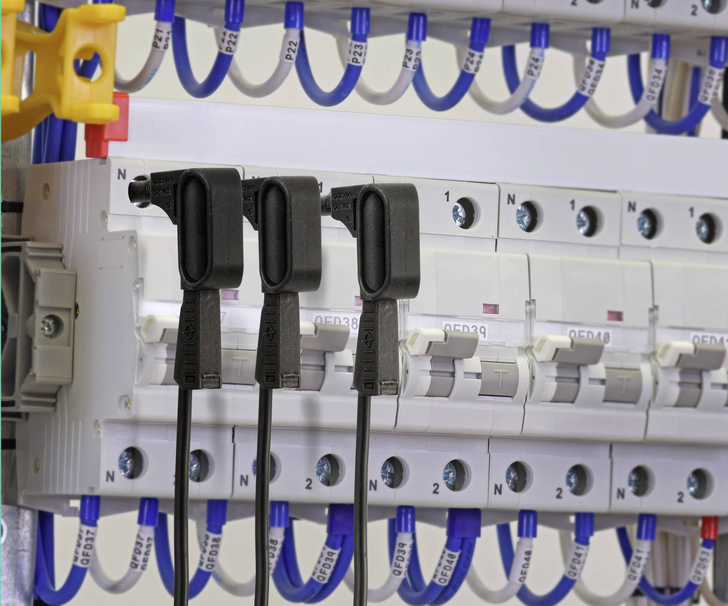 Drei schwarze Stromwandler, die an Sicherungsautomaten in einer Elektroverteilerschrank angeschlossen sind, mit blauen und weißen Kabeln, die darüber organisiert sind.