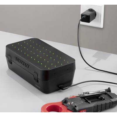 Schwarzes Batterieladegerät mit grünen Anzeigelichtern, das in eine Wandsteckdose eingestöpselt ist und ein Batteriepack auf einer Werkbank lädt.