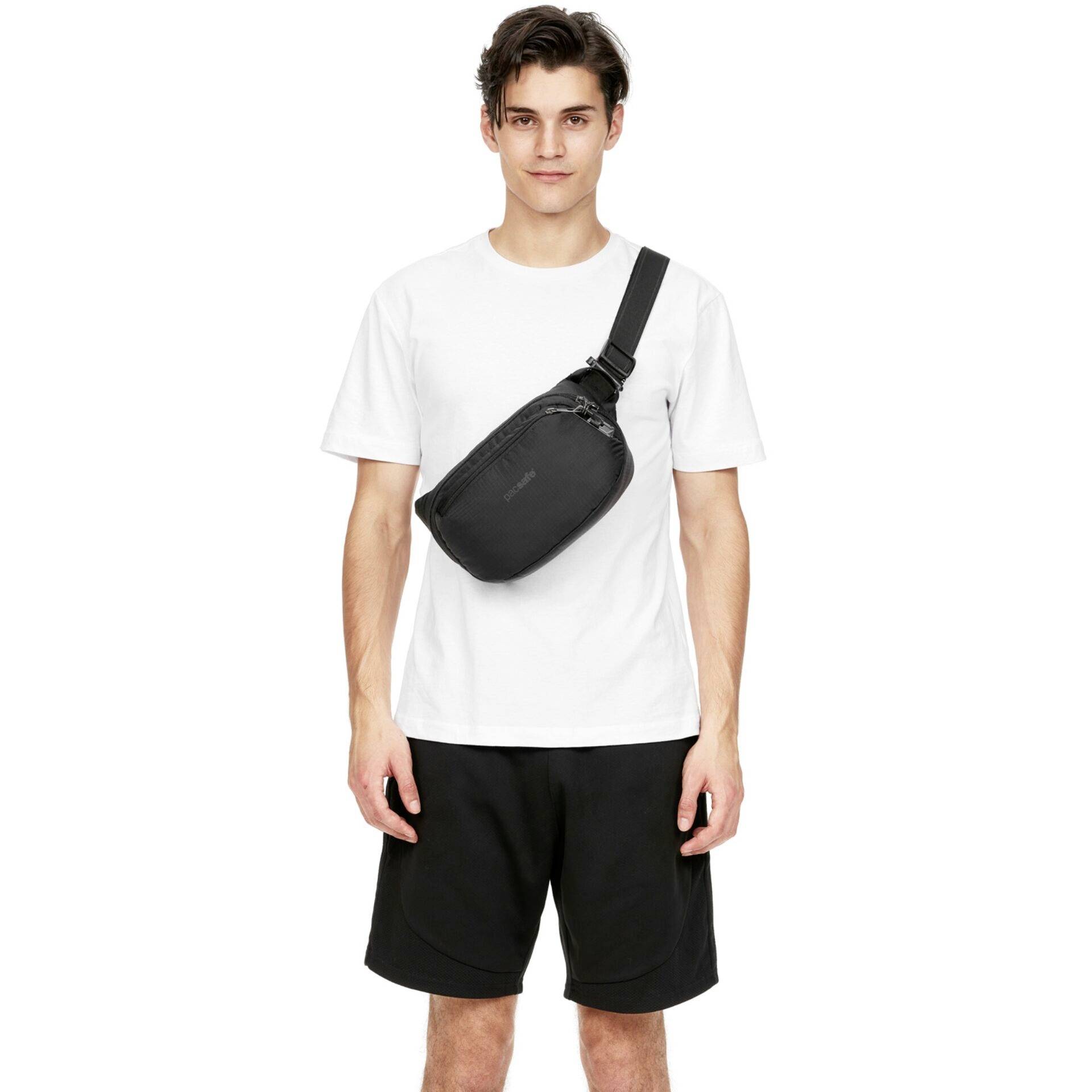 Eine Person steht und trägt ein weißes T-Shirt, schwarze Shorts und eine schwarze Umhängetasche. Der Hintergrund ist schlicht weiß.