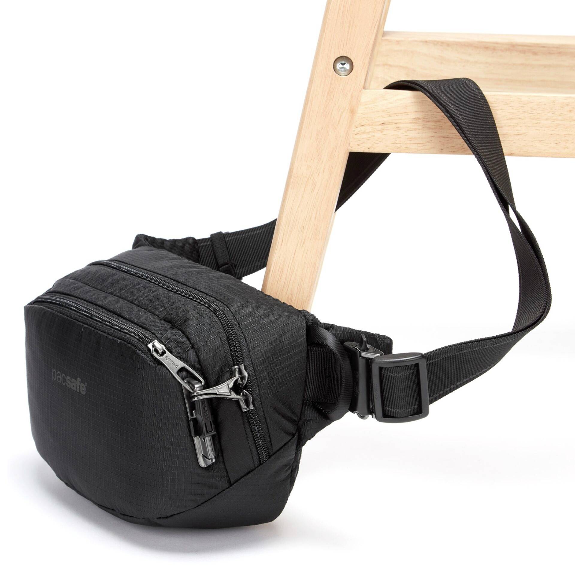 Eine kleine schwarze Tasche mit Reißverschlüssen ist mit ihrem verstellbaren Gurt an einem Stuhlbein aus Holz befestigt.