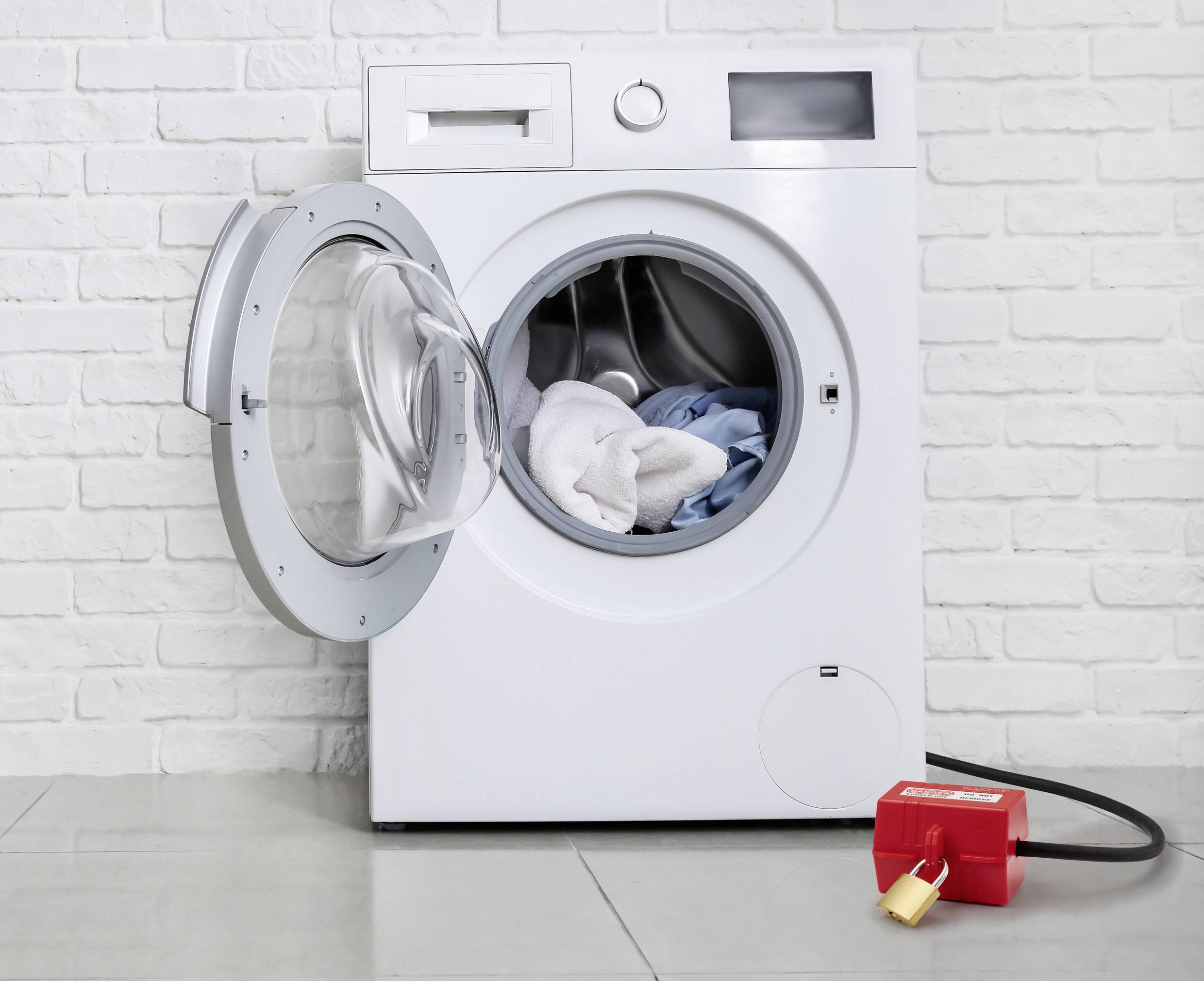Eine Frontlader-Waschmaschine mit offener Tür, in der Kleidungsstücke zu sehen sind. Ein roter Sicherungsmechanismus ist an seinem Stecker angebracht.