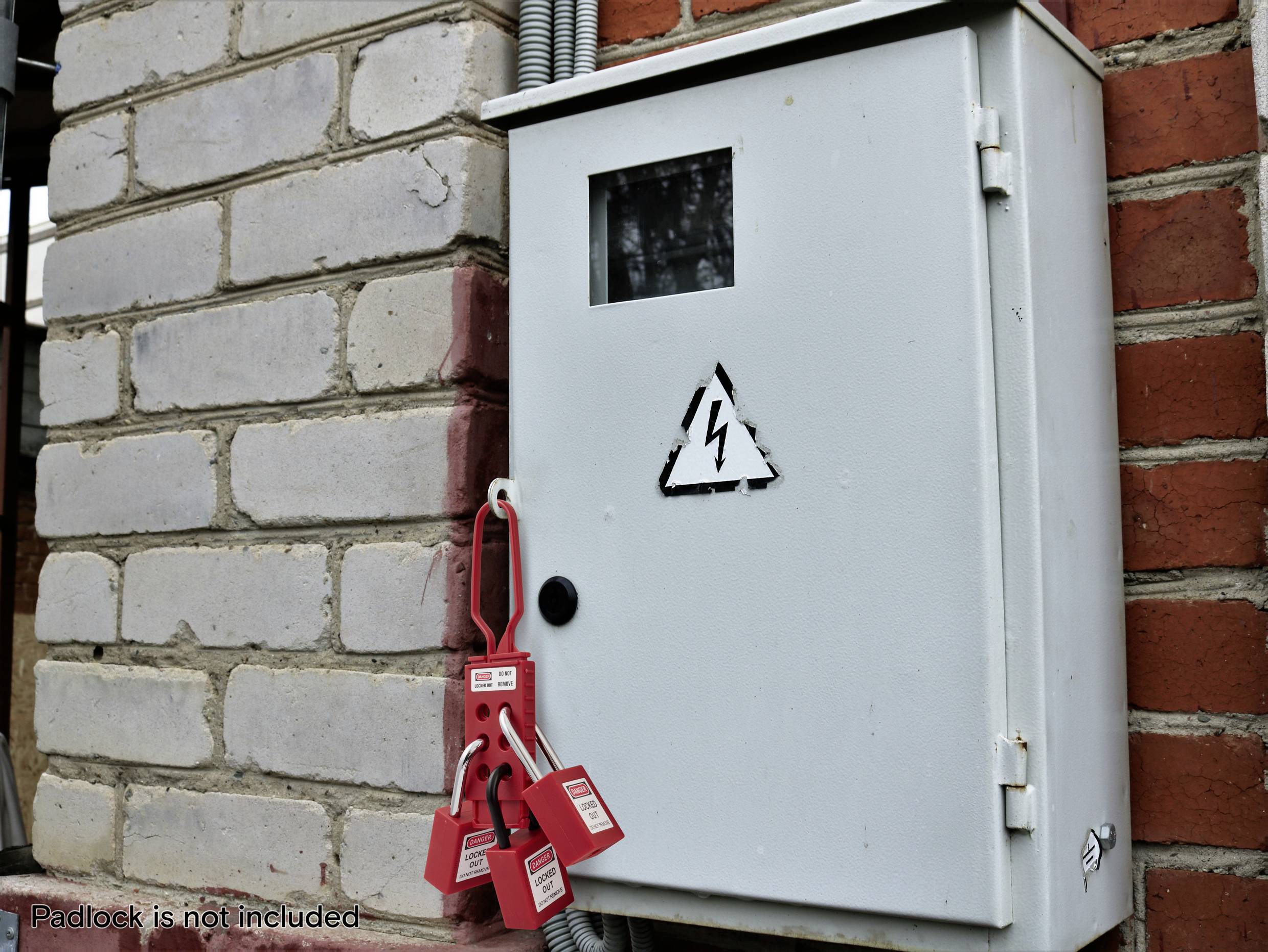Elektrische Schalttafel an einer Ziegelwand mit einem Warnschild. Mehrere rote Ausschluss-Sicherheitsetiketten hängen von einem Kabel, was auf Wartungsarbeiten oder eingeschränkten Zutritt hinweist.