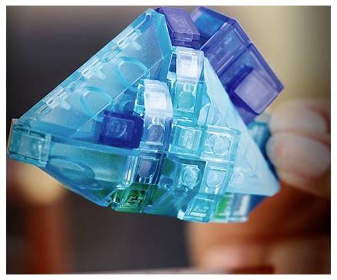 Eine Hand hält ein geometrisches Spielzeug aus ineinandergreifenden transparenten blauen und lila Plastikteilen und zeigt dessen komplexe Struktur und lebendigen Farben.