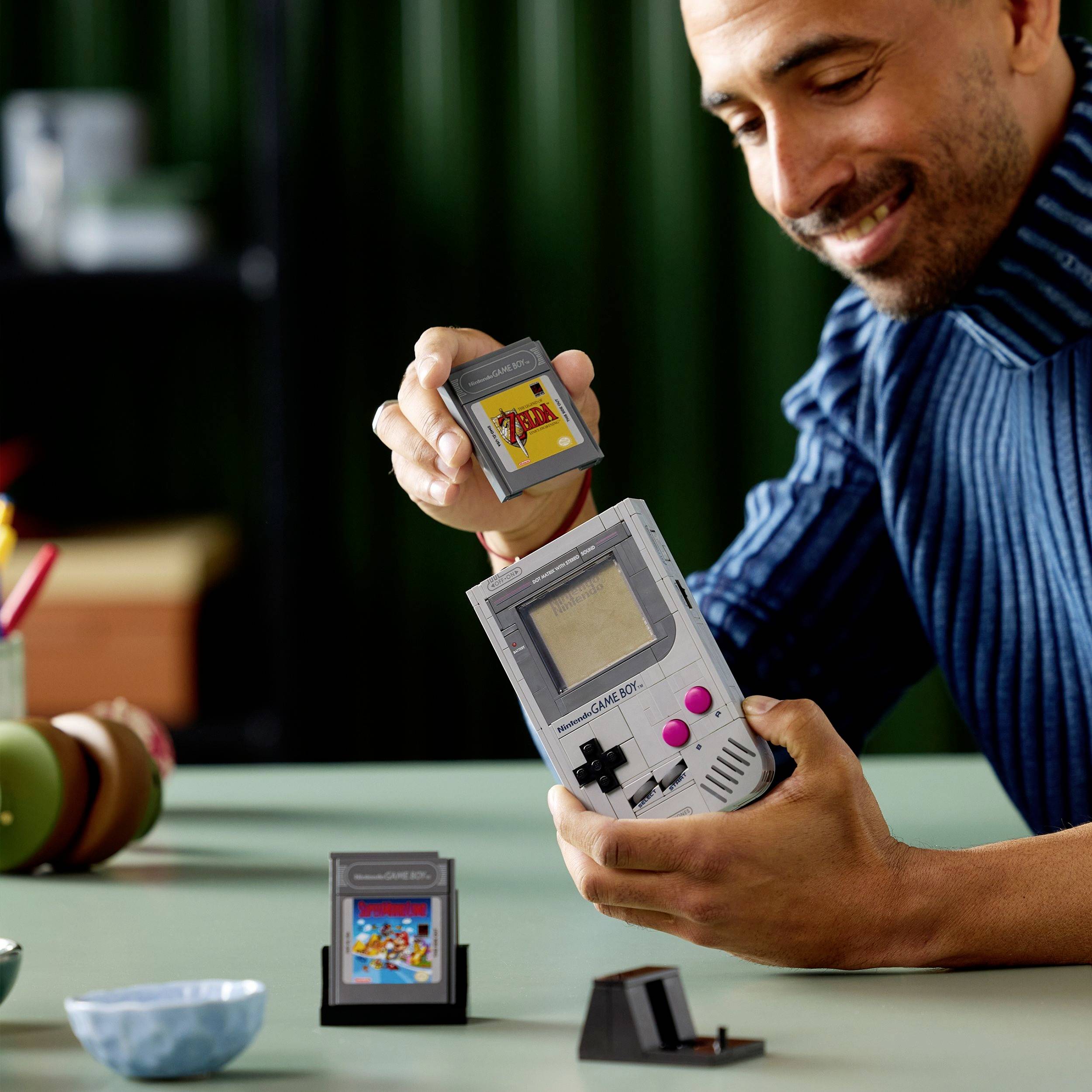 Eine Person lächelt, während sie eine Retro-Handheld-Spielkonsole und eine Spielpatrone hält und damit Freude an klassischen Videospielen andeutet.