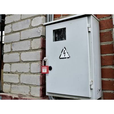 Elektrische Schalttafel mit einem 'Gefahr'-Symbol und mit einem roten Vorhängeschloss gesichert. An einer Ziegelwand montiert, was auf eingeschränkten Zugang aus Sicherheitsgründen hinweist.