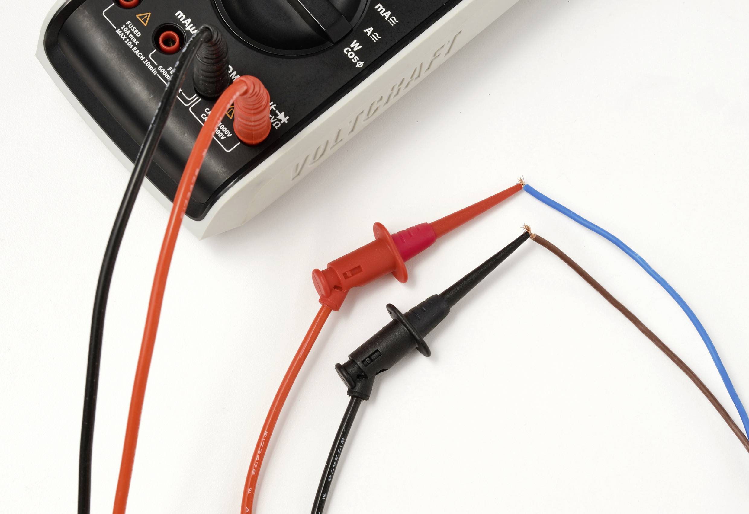 Ein digitales Multimeter mit roten und schwarzen Messspitzen ist an blaue und braune Kabel angeschlossen und zeigt eine Test- oder Messanordnung.