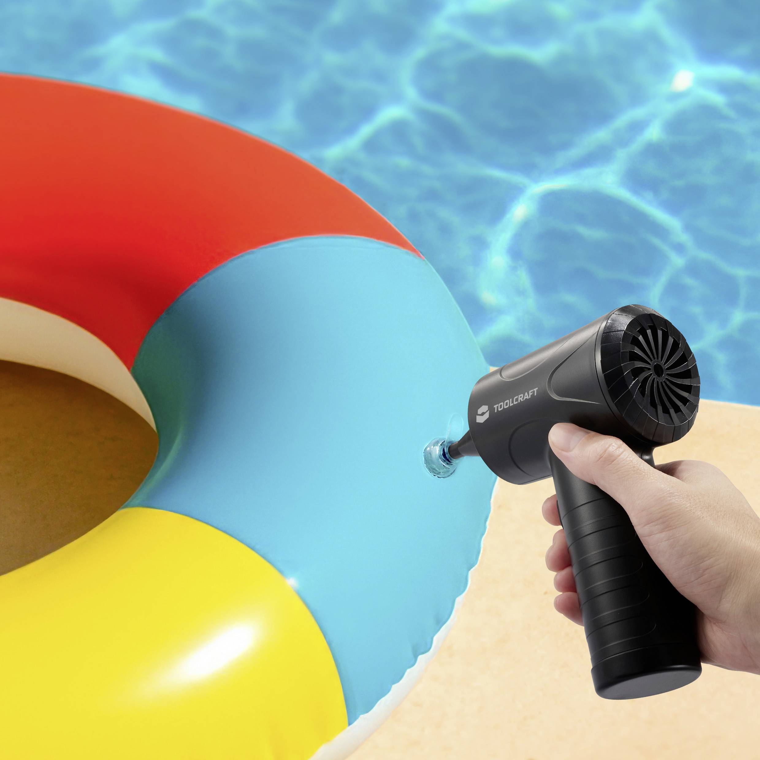Eine Person bläst eine bunte Luftmatratze mit einer elektrischen Luftpumpe neben einem hellblauen Swimmingpool auf.