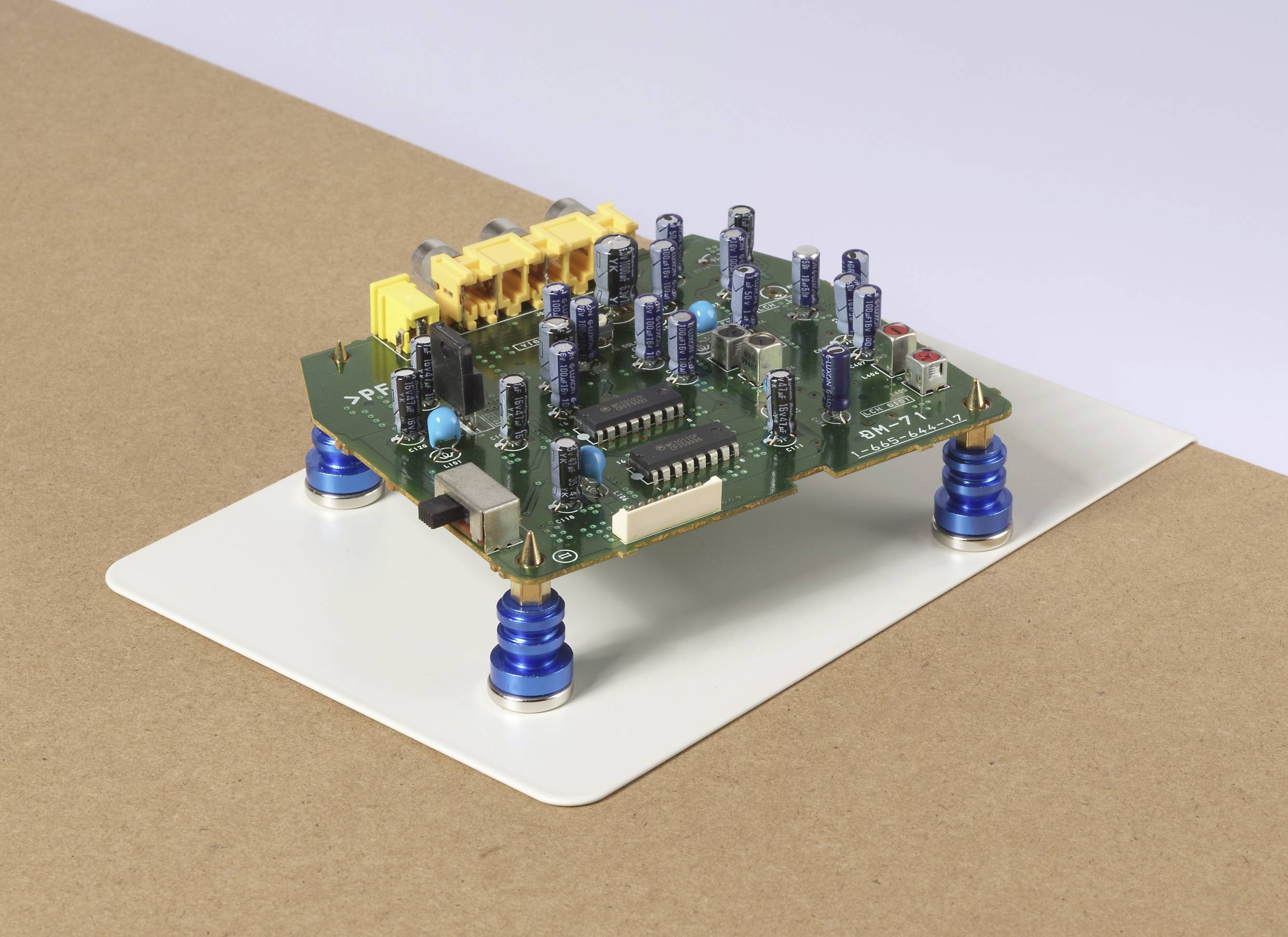 Eine kleine elektronische Leiterplatte mit verschiedenen Kondensatoren und Komponenten ist auf einer weißen Plattform mit blauen Schraubenfedern montiert.