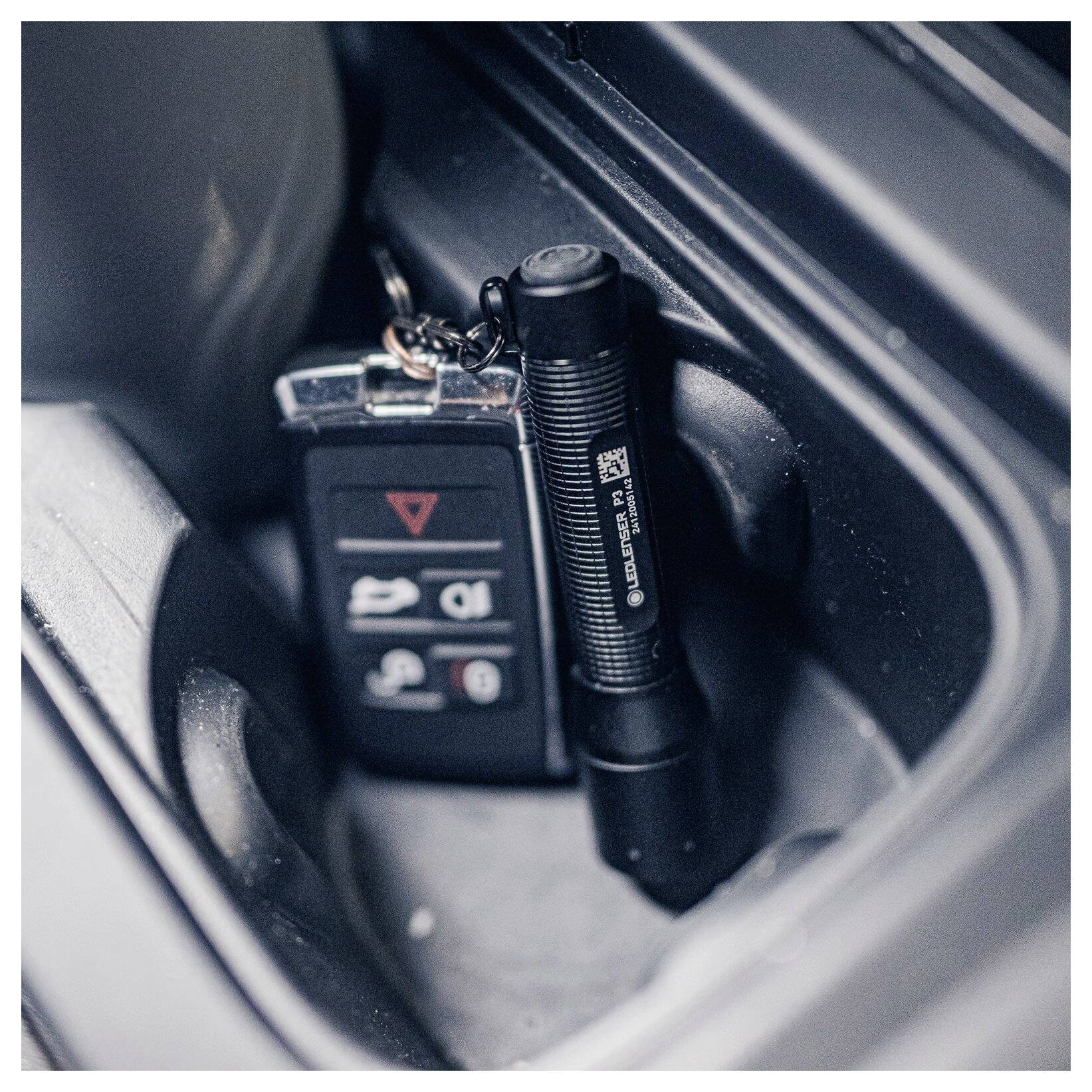 Nahaufnahme der Mittelkonsole eines Autos mit einem Schlüsselanhänger und einer kleinen Taschenlampe, die in einem Stauraum verstaut sind.