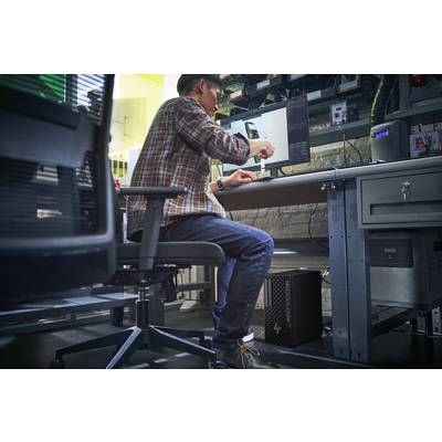 Eine Person sitzt an einem Arbeitsplatz und verwendet einen digitalen Stift an einem Computer, wobei technische Ausrüstung sichtbar ist, was auf ein Elektroniklabor hinweist.