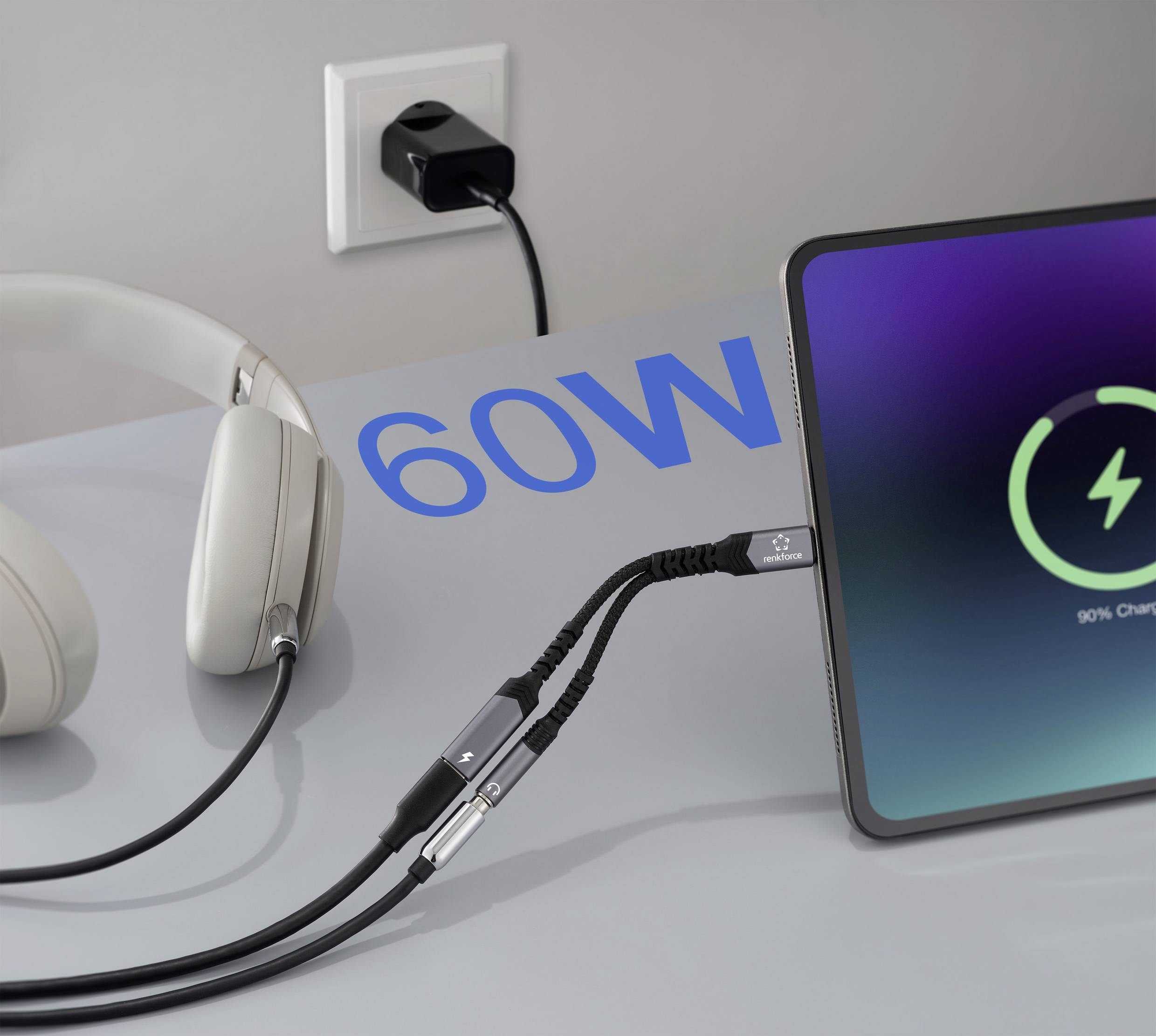 Ein Tablet mit der Anzeige "90% geladen" ist in eine Steckdose mit einem 60-Watt-Ladegerät eingesteckt. Ein Kopfhörerpaar befindet sich in der Nähe.