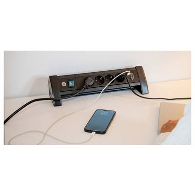 Ein Smartphone wird auf einem Schreibtisch über eine schwarze Steckerleiste mit mehreren Steckplätzen und Kabeln aufgeladen.
