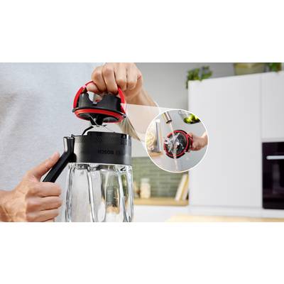Eine Person hält einen Standmixer in einer Küche und demonstriert die einfache Reinigung, indem sie den Deckel unter einem Wasserhahn abspült, wie in einem kleinen Einschub gezeigt.