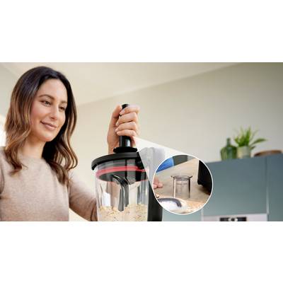 Eine Person schiebt Lebensmittel durch einen schwarz-transparenten Küchenmixer. Eine Nahaufnahme zeigt einen kleinen runden Behälter daneben.