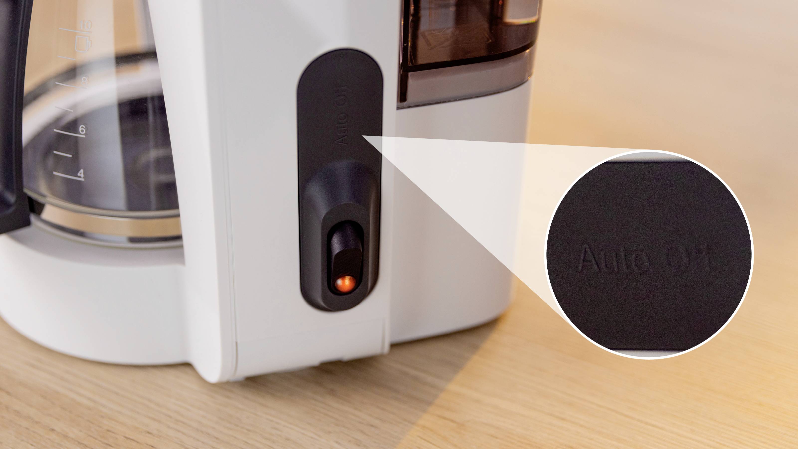 Ein weißer Kaffeemaschine mit einem beleuchteten Netzschalter mit der Aufschrift "Automatische Abschaltung" auf einer Holzoberfläche.