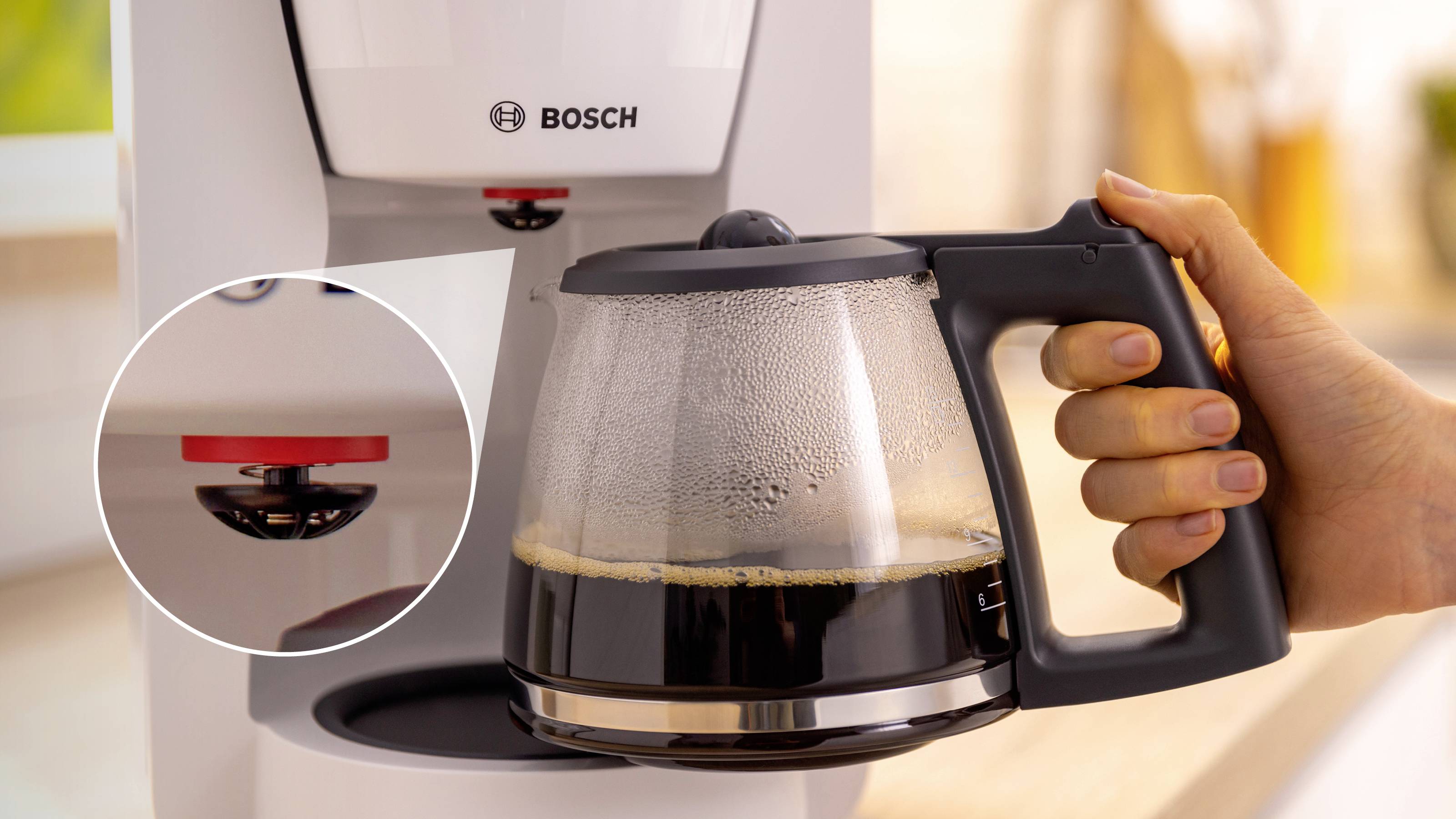 Eine Hand hält eine Glaskanne mit gebrühtem Kaffee, die unter einer Bosch-Kaffeemaschine positioniert ist, mit einer Nahaufnahme der Tropfstopp-Funktion.