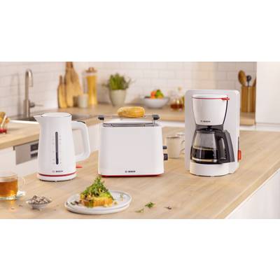 Eine moderne Kücheneinrichtung mit einem weißen Wasserkocher, einem Toaster mit einem Bagel und einer Kaffeemaschine auf einer Holzarbeitsplatte. Teller mit Speisen und eine Teetasse befinden sich in der Nähe.