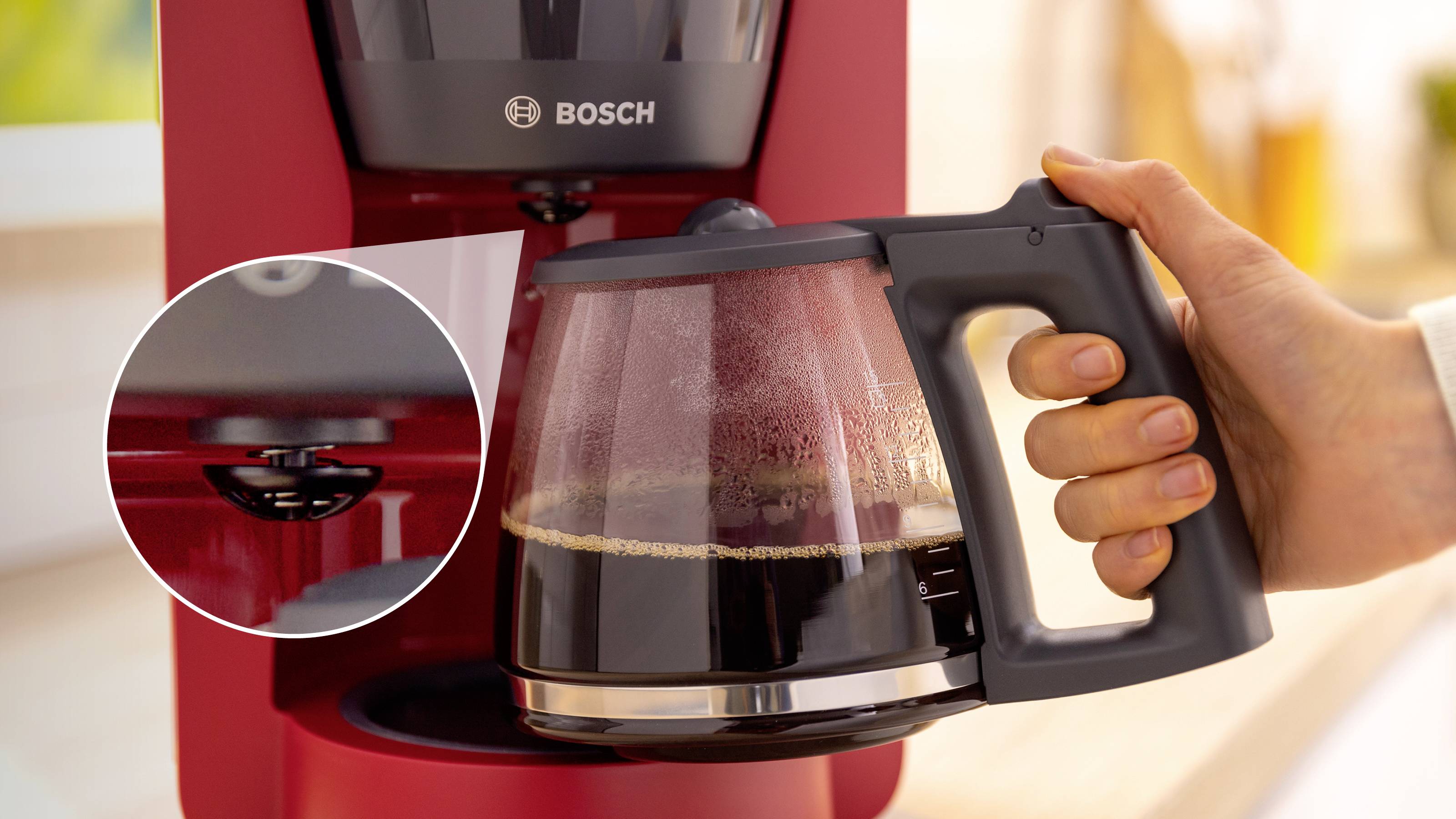 Eine rote Kaffeemaschine mit einer Hand, die eine Glaskanne hält, die zur Hälfte mit Kaffee gefüllt ist; ein Ausschnitt zeigt eine Nahaufnahme der Wasserdüse.