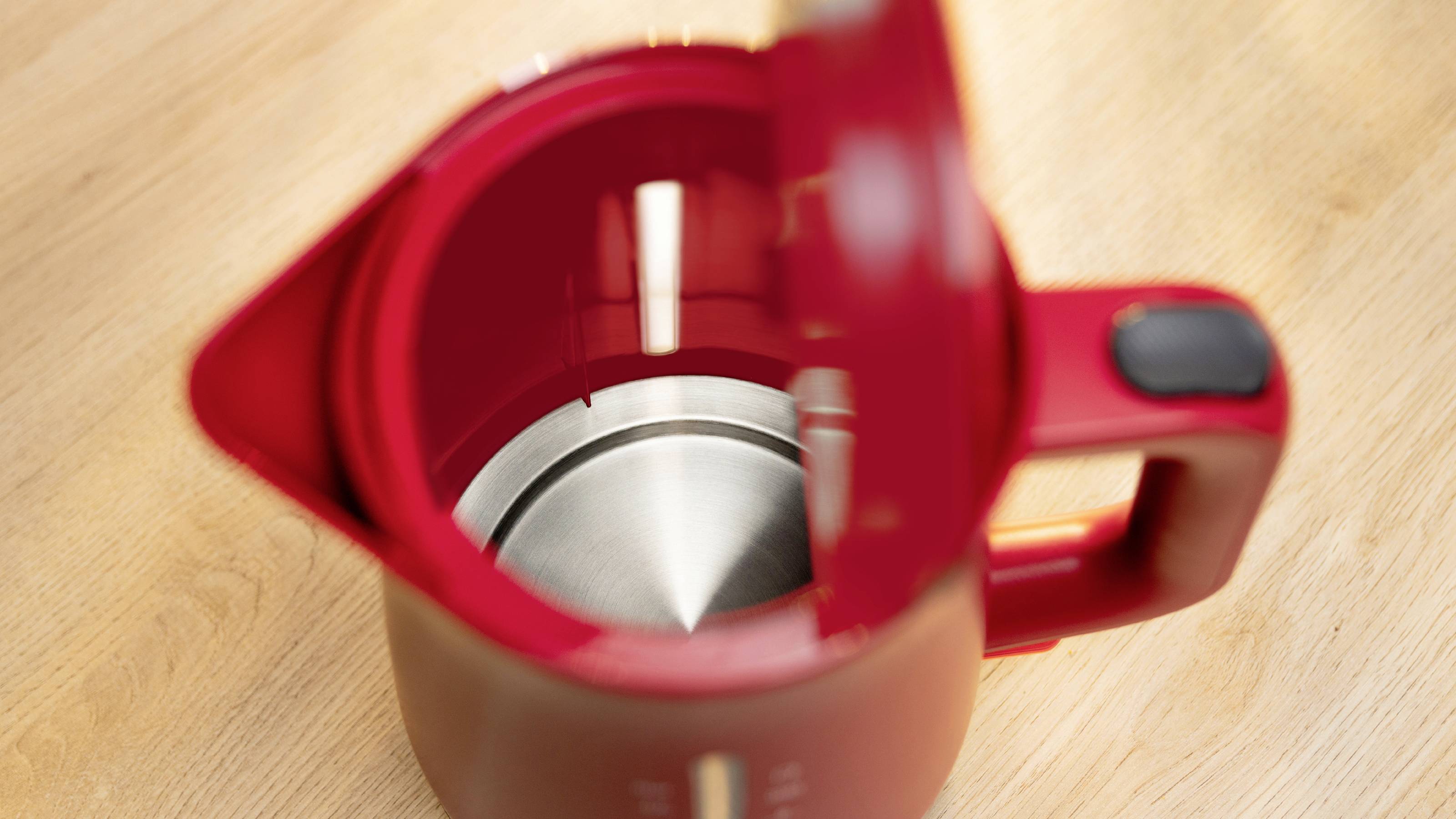 Ein roter elektrischer Wasserkocher mit geöffnetem Deckel auf einer Holzoberfläche, der ein Innenleben aus Edelstahl zeigt.