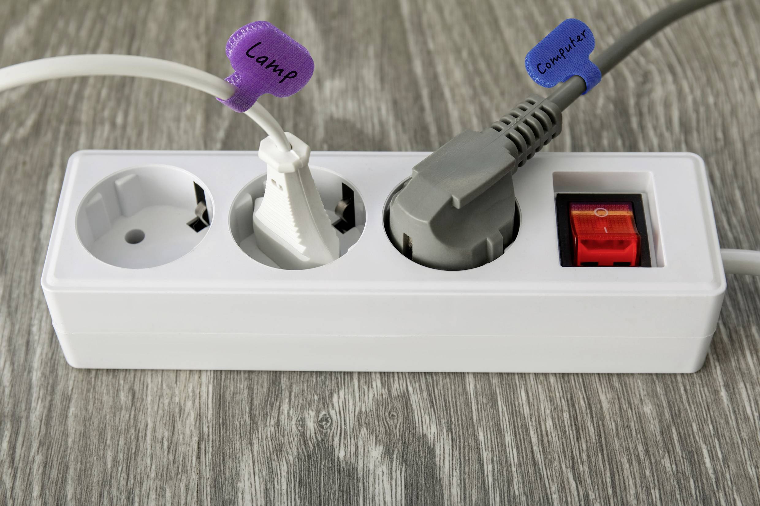 Eine Steckdosenleiste mit zwei Steckdosen, die mit "Lampe" und "Computer" beschriftet sind, ist angeschlossen. Sie steht auf einer Holzoberfläche.