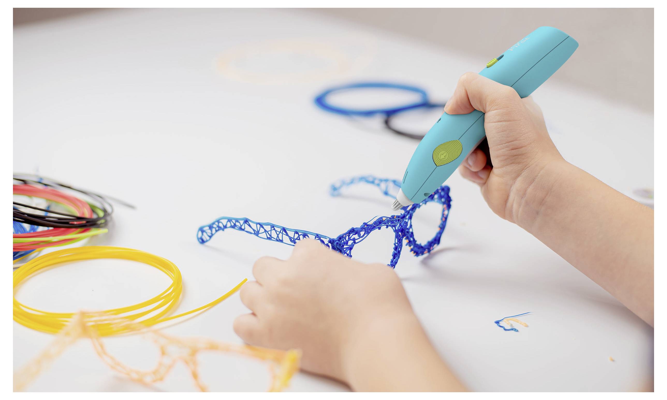 Ein Kind verwendet einen 3D-Druckstift, um auf einem Tisch blaue Brillengestelle zu erstellen, wobei verschiedenfarbige Filamentspulen in der Nähe liegen.