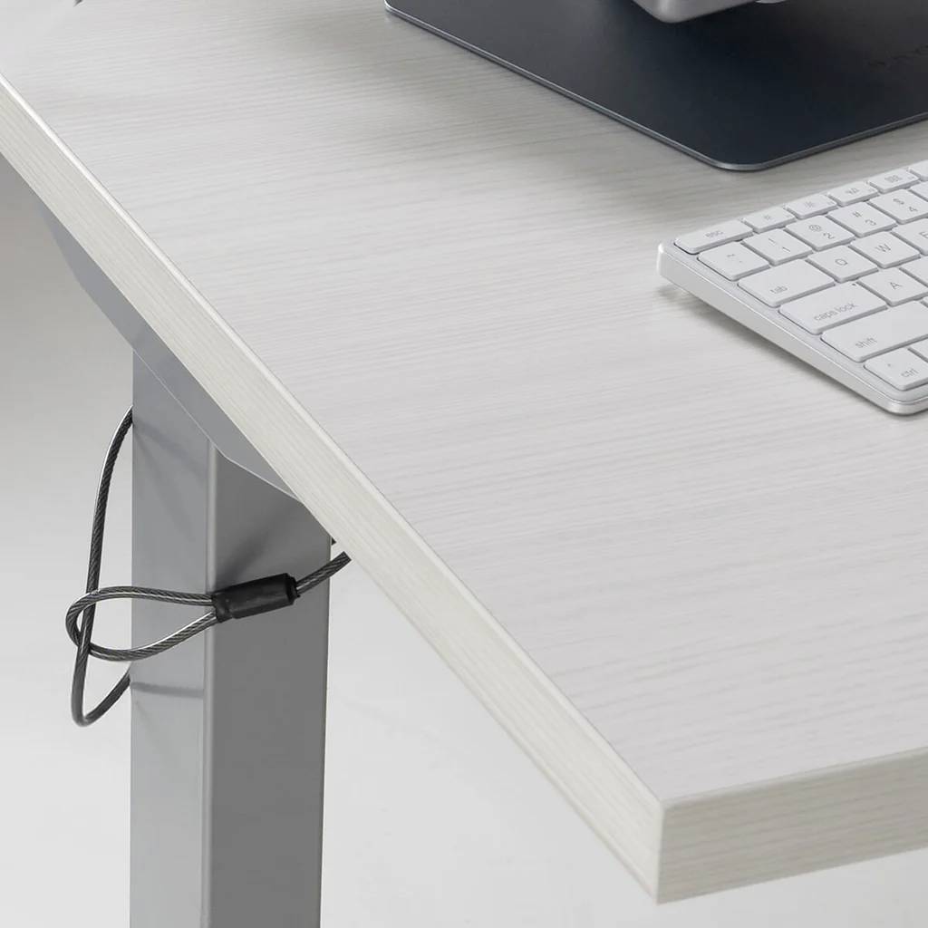 Ein höhenverstellbarer Schreibtisch mit einem Kabelmanagement-System, auf dem ein Teil einer Tastatur und eines Laptops zu sehen ist und der die Organisation des Arbeitsplatzes betont.