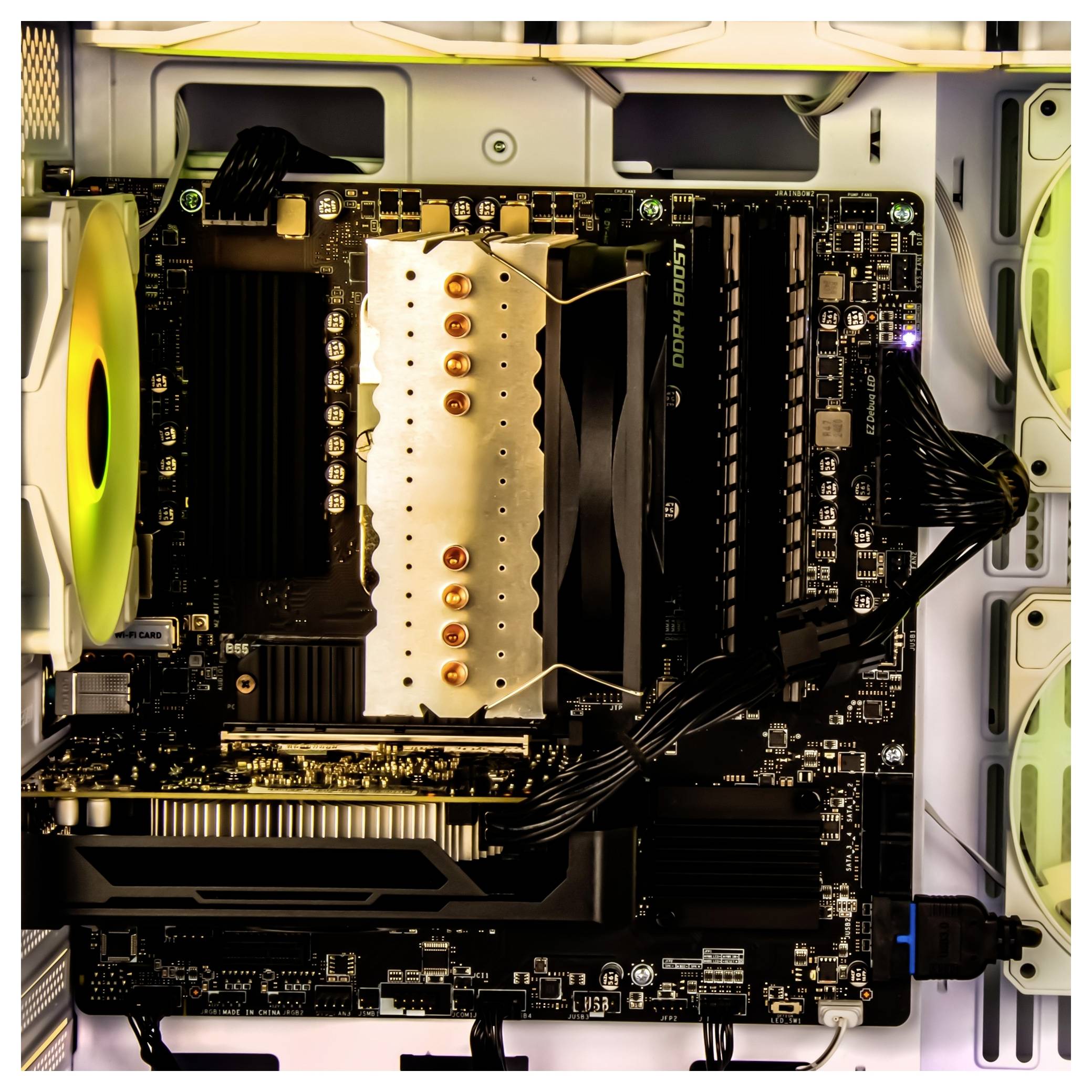 Eine Computermotherboard mit einem großen silbernen CPU-Kühler und sichtbaren Komponenten in einem Gehäuse, die Kühlung und Verkabelungslayout hervorheben.