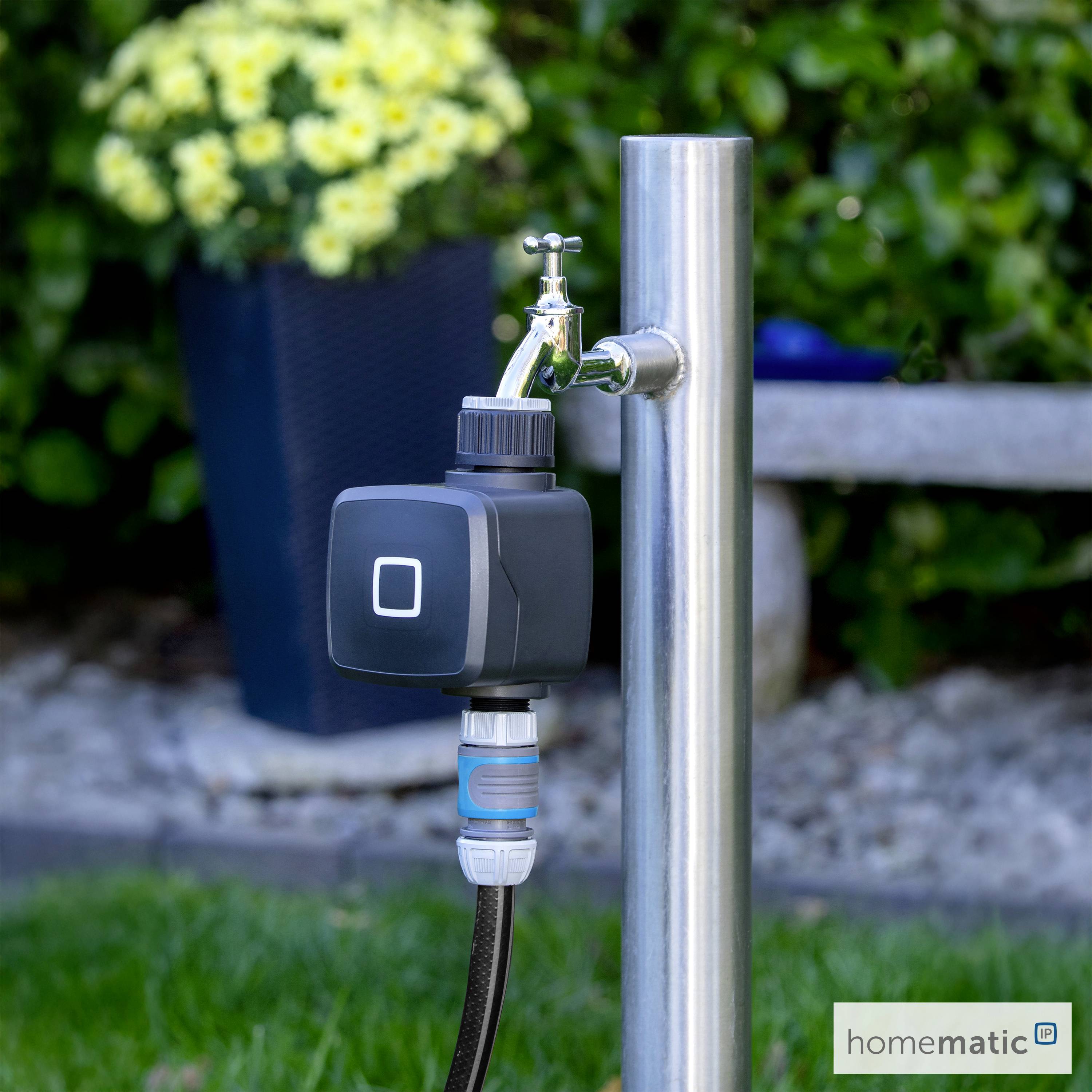 Ein intelligentes Wasserventil an einem Stahlgartenhahn, umgeben von grünen Pflanzen und Blumen, das moderne Gartentechnologie veranschaulicht.