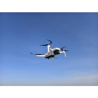 Ein weißer Quadrocopter-Drohne, die vor einem klaren blauen Himmel fliegt und dessen Propeller und Kamera präsentiert, was moderne Luftfahrttechnologie veranschaulicht.