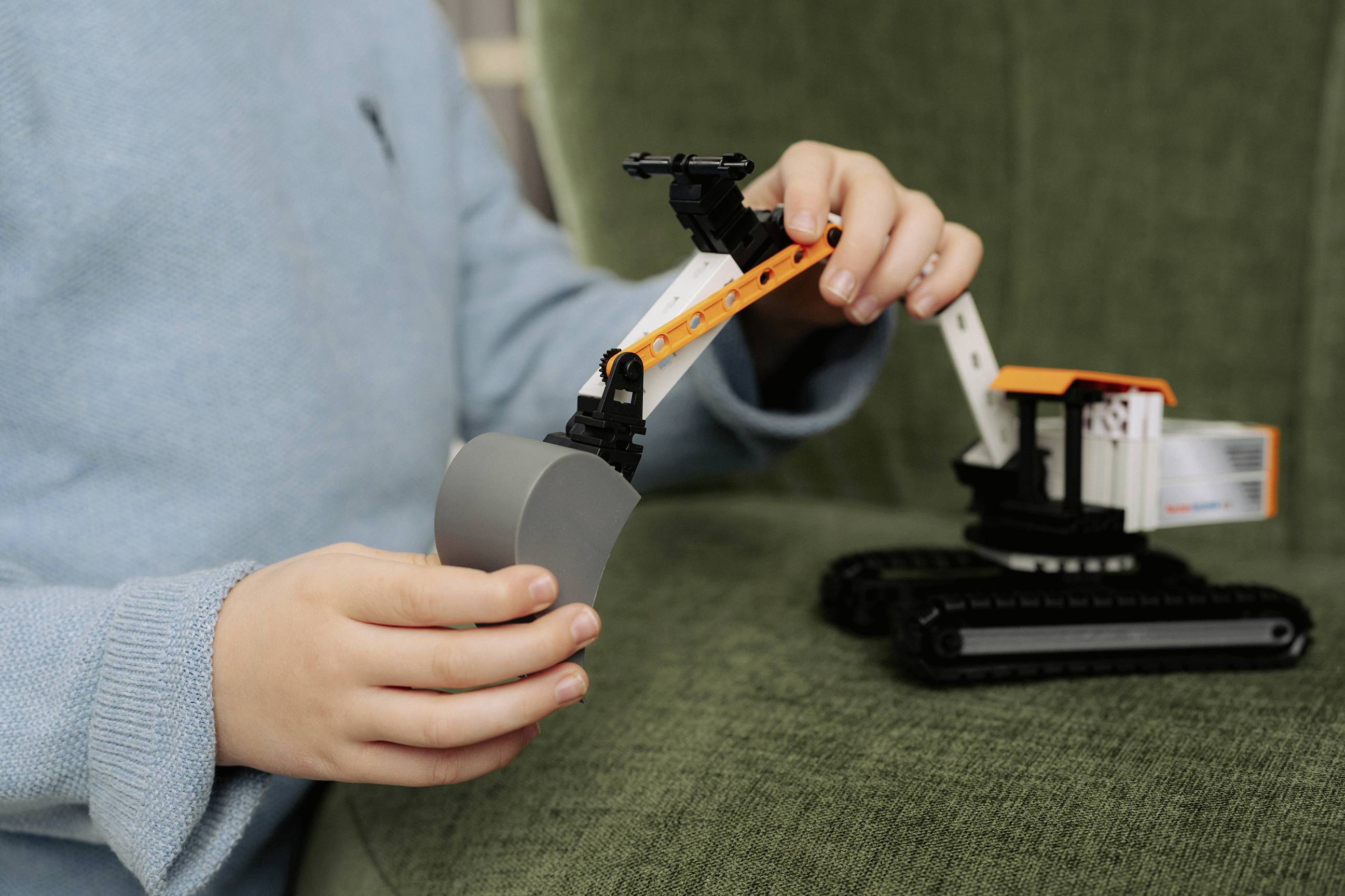 Ein Kind in einem blauen Pullover baut einen kleinen Spielzeug-Bagger auf einer grünen Couch zusammen.