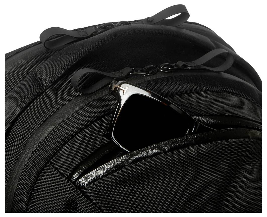 Schwarzer Rucksack mit Sonnenbrille, die teilweise in eine äußere Reißverschlusstasche gesteckt ist.