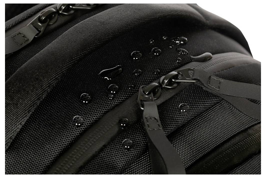 Nahaufnahme eines schwarzen Rucksacks mit Wassertropfen auf seinem wasserbeständigen Stoff und Reißverschlüssen.