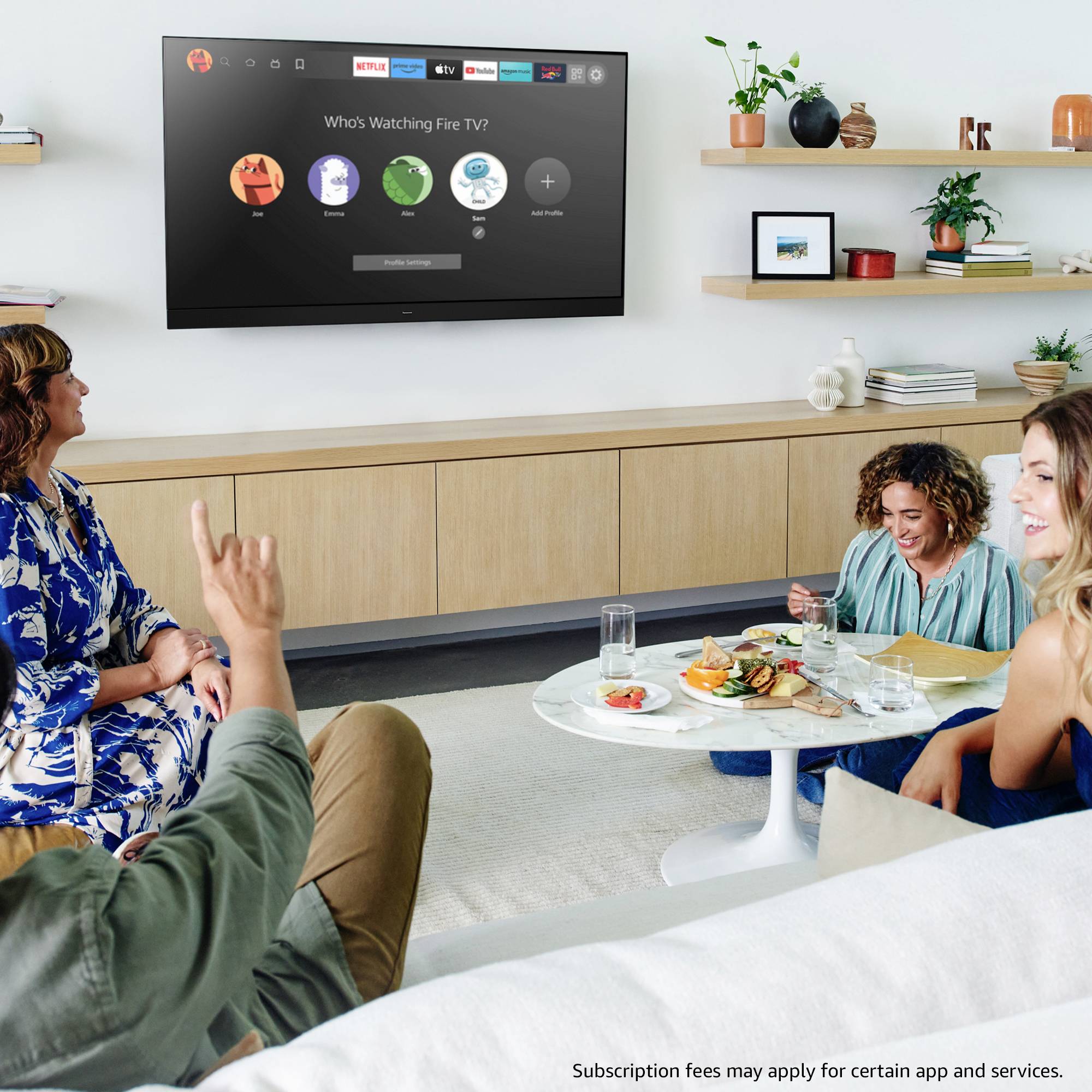 Eine Gruppe von vier Personen, die auf einem Sofa sitzen und einen Fernseher mit einem "Who's Watching Fire TV?"-Bildschirm in einer gemütlichen Wohnzimmeratmosphäre betrachten.