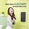 A woman in a bathroom smiles while holding an electric toothbrush. The text reads 'Weil dein Lächeln ansteckend ist' (Because your smile is contagious).<br><br>(Note: The text is already in German, so no translation is needed.)