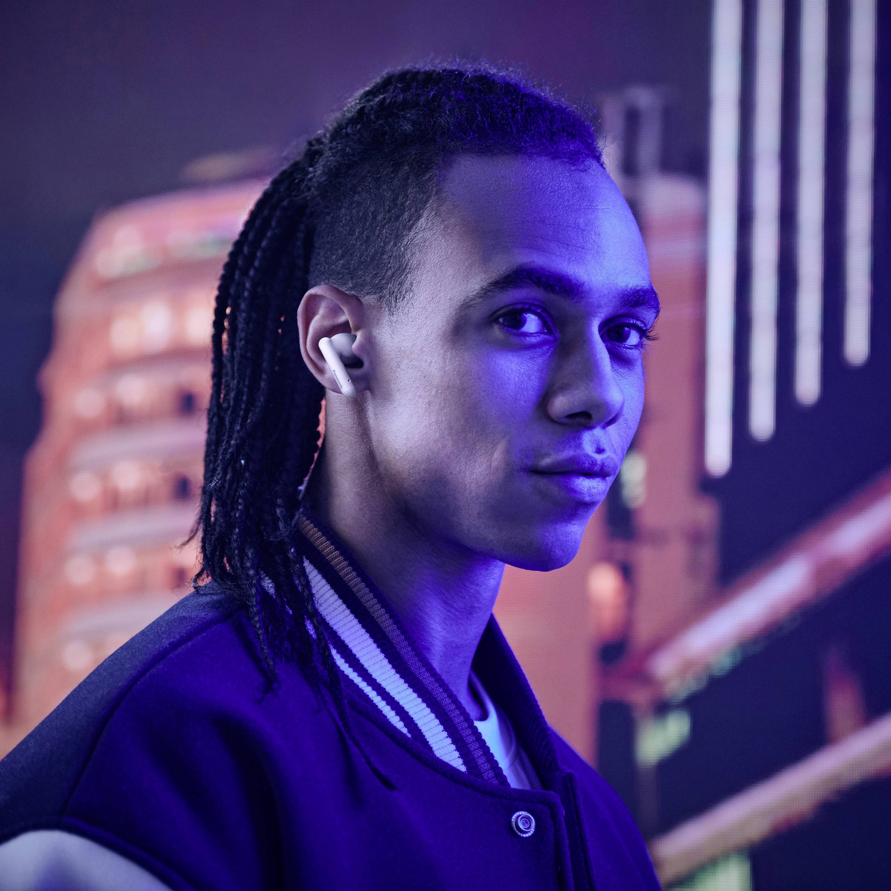 Eine Person mit einer Varsity-Jacke und Kopfhörern blickt über ihre Schulter in einer nächtlichen Stadtlandschaft, mit bunten Neonlichtern im Hintergrund.