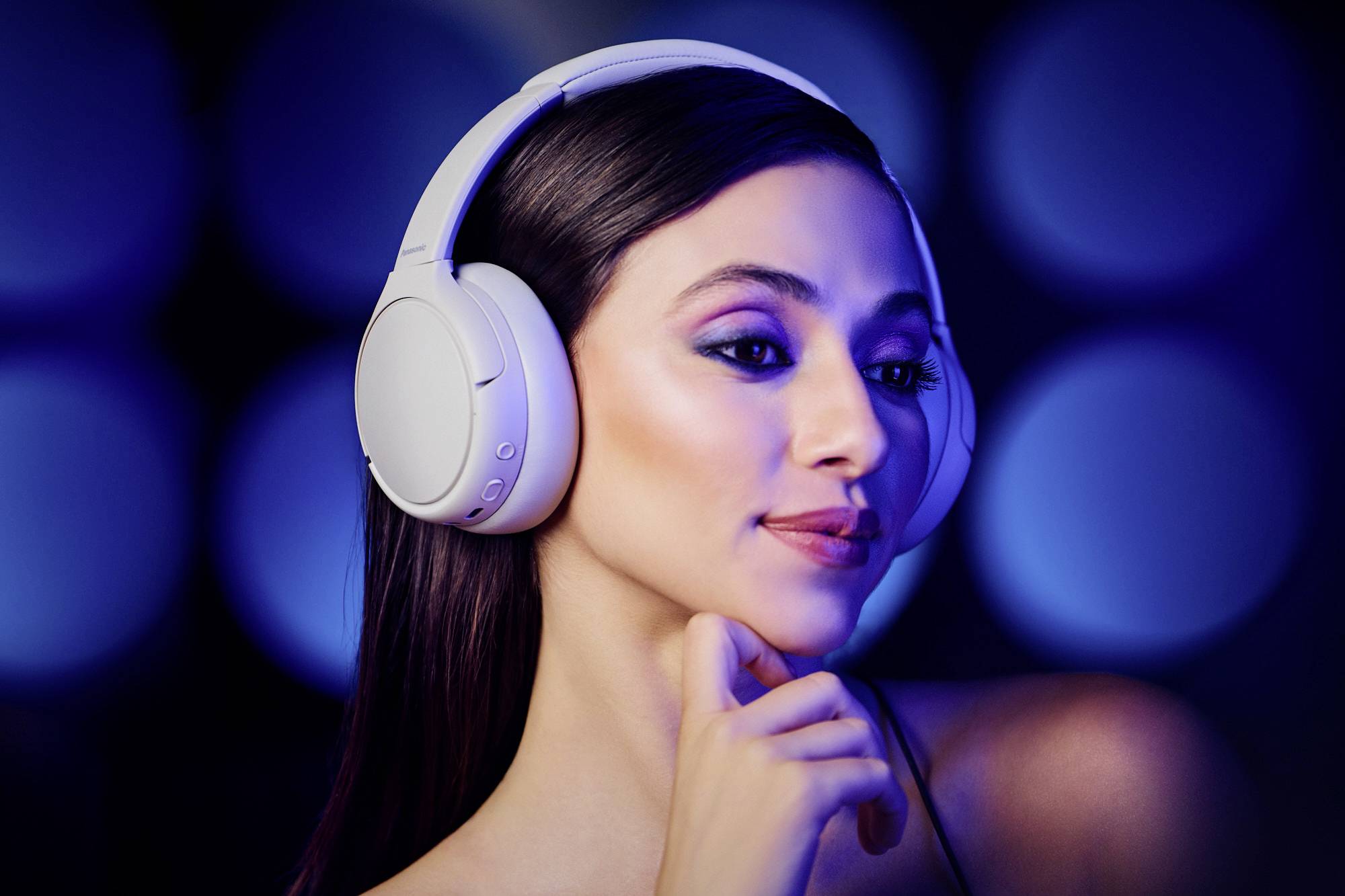 Eine Person mit Over-Ear-Kopfhörern genießt Musik mit einem heiteren Gesichtsausdruck vor einem unscharfen blauen Hintergrund, was ein Gefühl von Ruhe vermittelt.