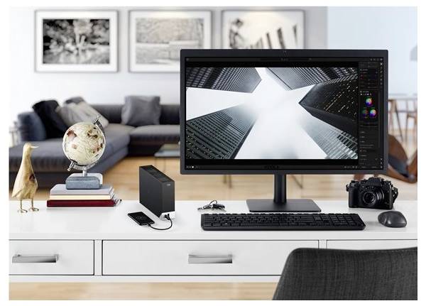 Ein moderner Arbeitsplatz mit einem Computermonitor, der Wolkenkratzer zeigt, mit einem Globus, Büchern und einer Kamera auf dem Schreibtisch in einem stilvollen Raum.