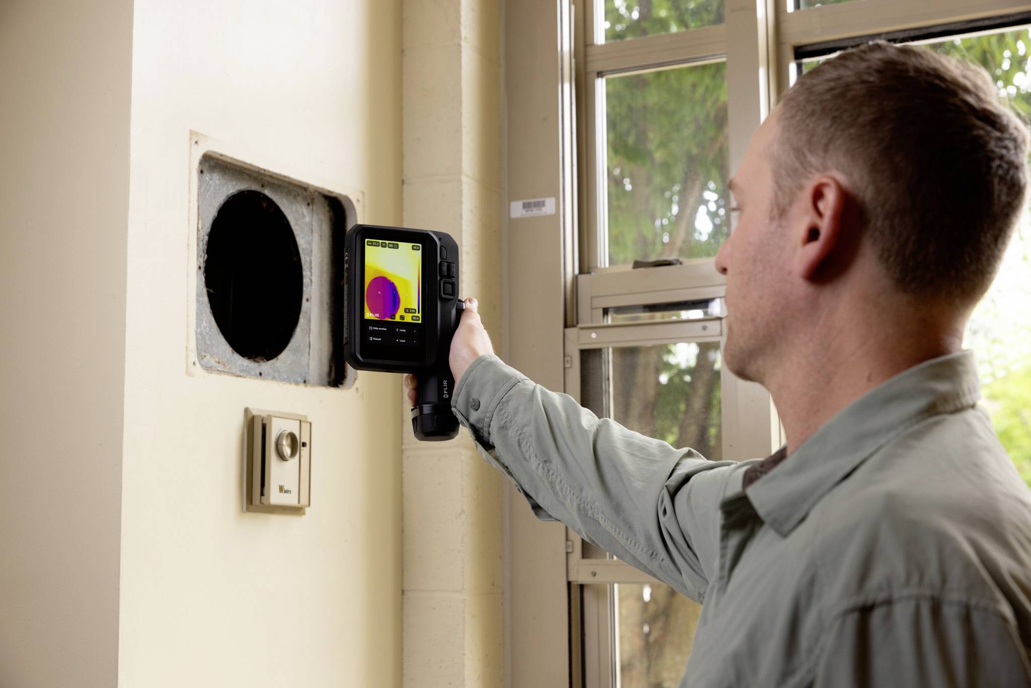 Eine Person verwendet eine Wärmebildkamera, um eine Wandbelüftung zu untersuchen und Temperaturunterschiede zu analysieren.