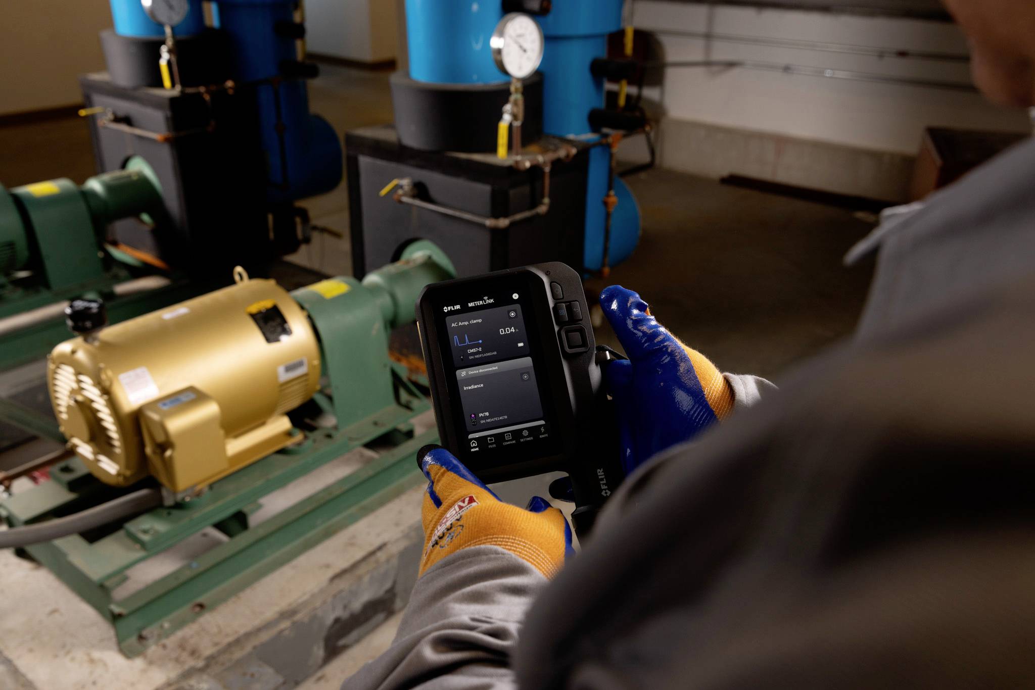 Eine Person mit Handschuhen bedient ein Gerät in einem Maschinenraum und überwacht Ausrüstung mit Messgeräten und Rohrleitungen, die im Hintergrund sichtbar sind.