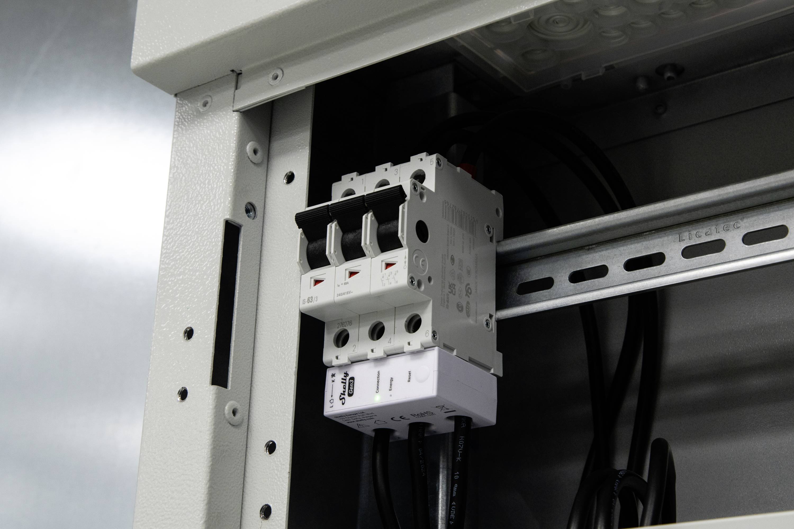 Eine Nahaufnahme eines elektrischen Sicherungsautomaten, der an einer Metallplatte in einem industriellen Gehäuse montiert ist und drei Schalter zeigt.