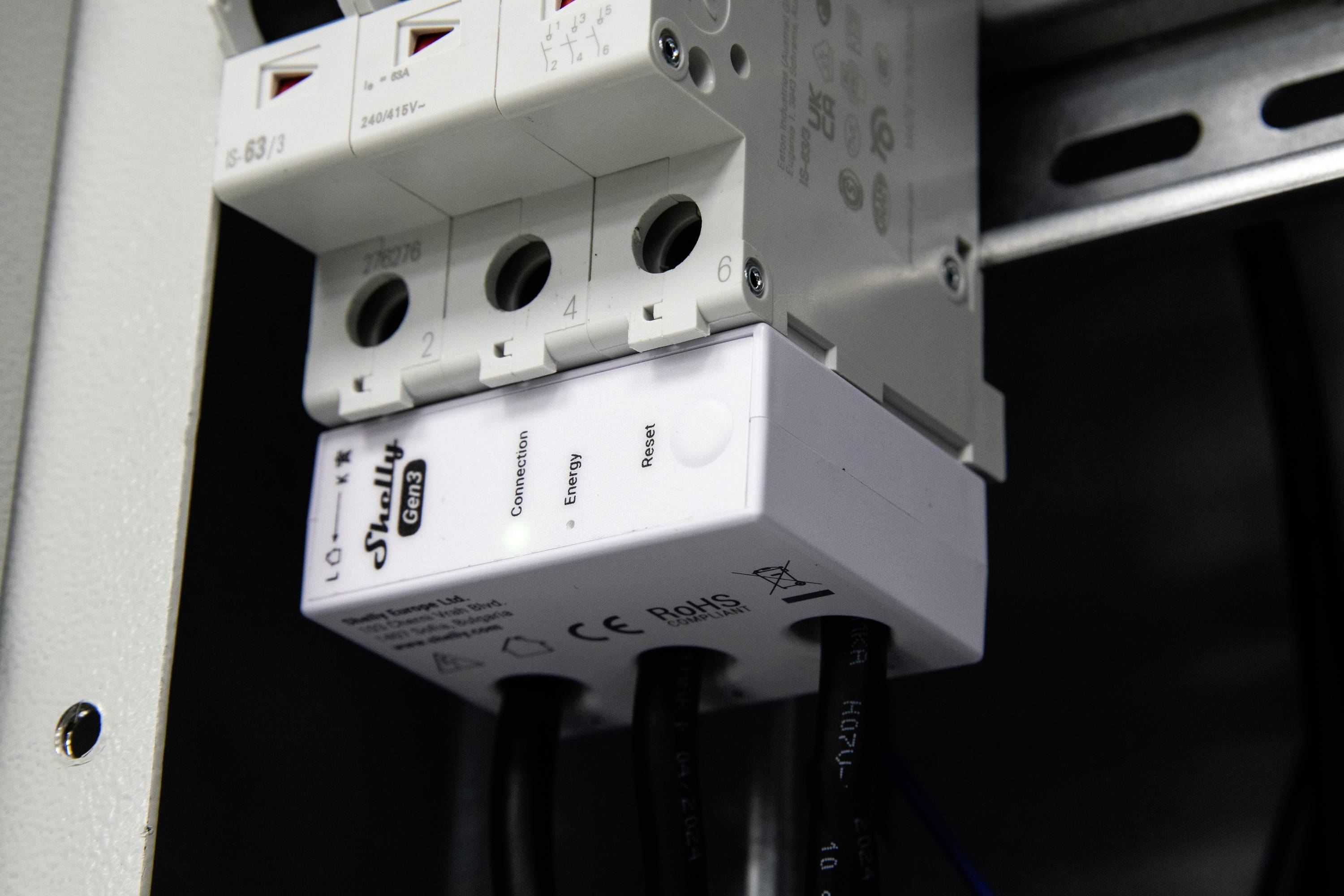 'Nahaufnahme eines Überspannungsschutzes in einer Elektroverteilanlage mit angeschlossenen Kabeln, die Betriebsmodus-Anzeigen und Sicherheitszertifizierungen zeigen.'