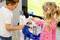 Zwei Kinder spielen mit einer Spielzeug-Rennstrecke und lenken ein Auto durch eine blaue Schleife. Sie sind konzentriert und teilen das spielerische Erlebnis.