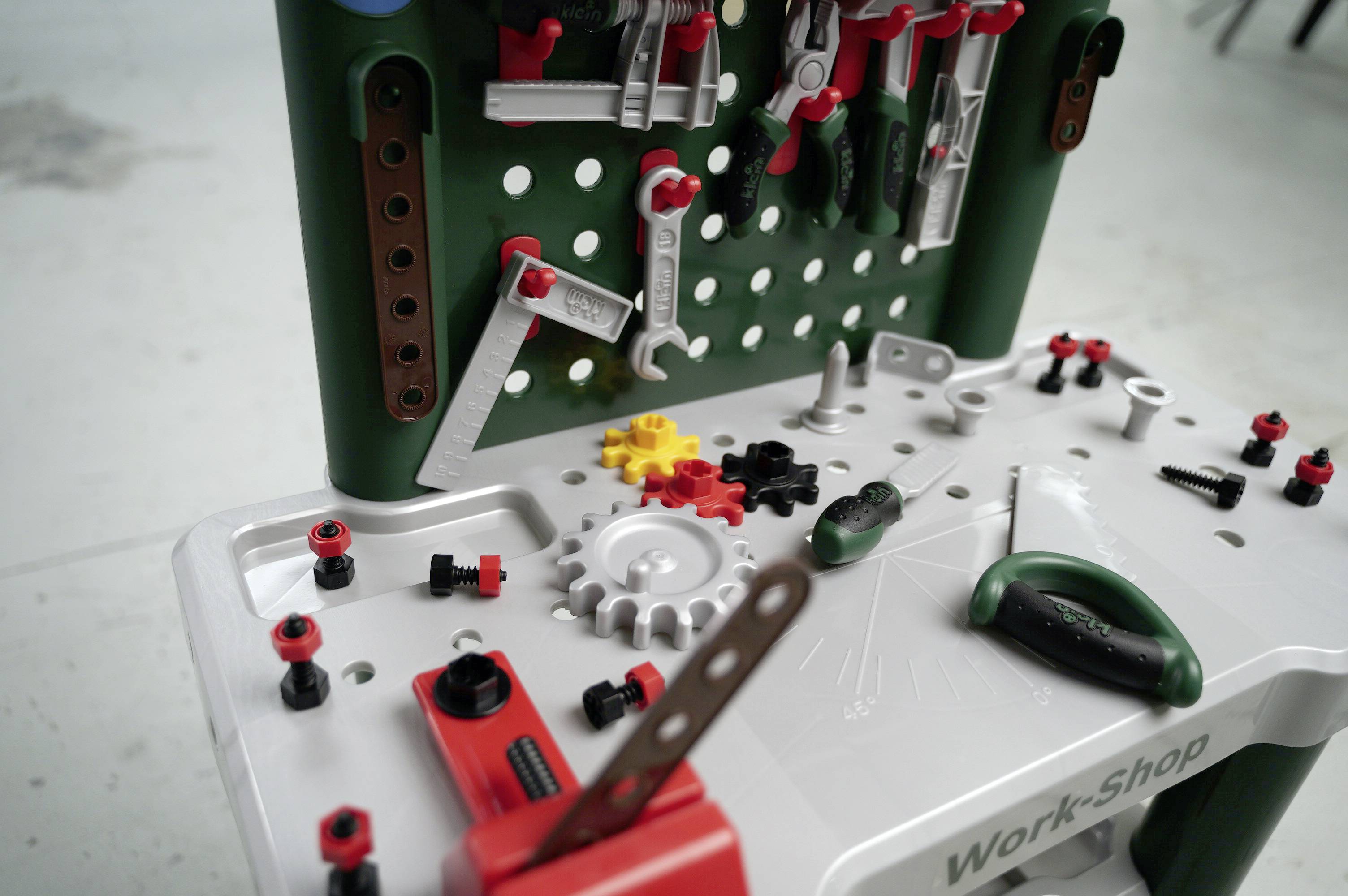 Miniatur-Werkstatt-Set mit Spielzeugwerkzeugen und Zahnrädern, auf einer weißen Werkbank angeordnet.